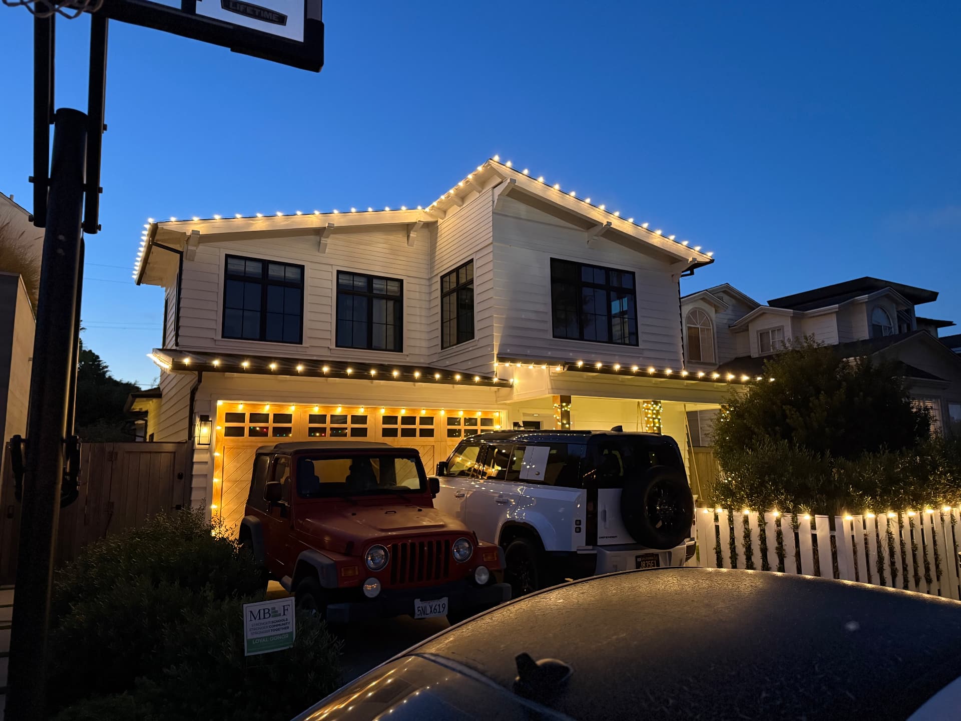Coastal home with warm white roofline lights and lit garage trim at dusk