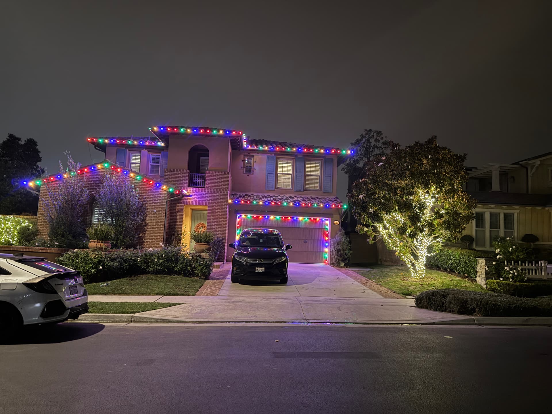 Two-story home outlined in multicolor holiday lighting with a lit front tree