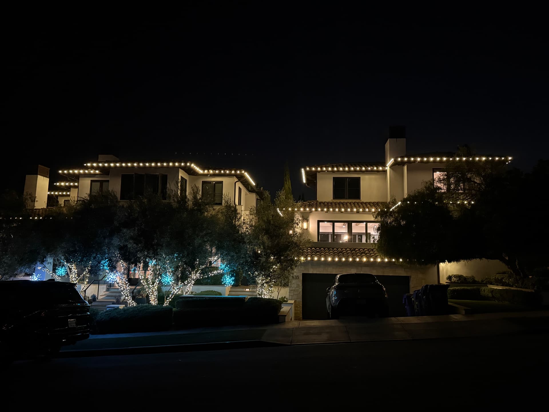 Warm white roofline holiday lighting on a Mediterranean estate with lit olive trees