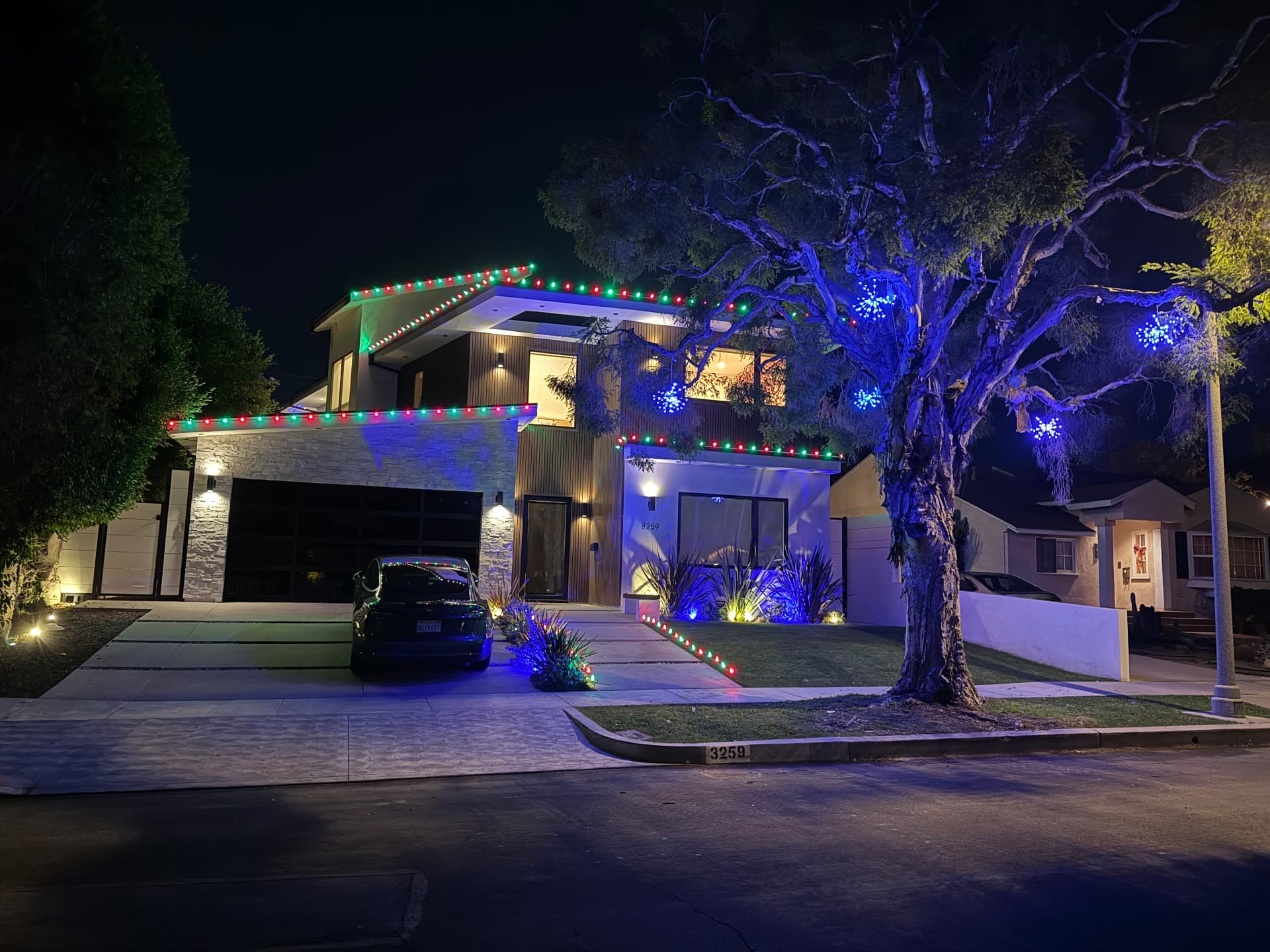 Modern home with red and green roofline lighting and blue-lit landscape trees
