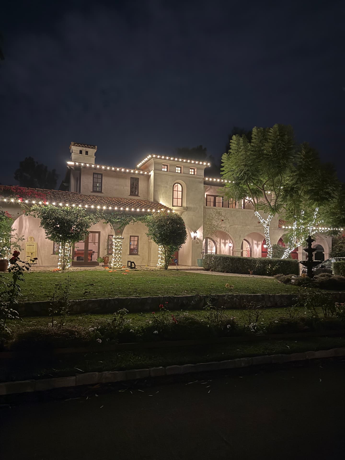 Spanish-style estate outlined in warm white lighting with lit arches and trees